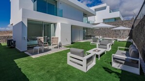 A modern house with a spacious outdoor patio featuring white furniture and a well-maintained lawn.
