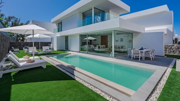 A modern two-story house with a swimming pool, outdoor seating, and a stone wall.