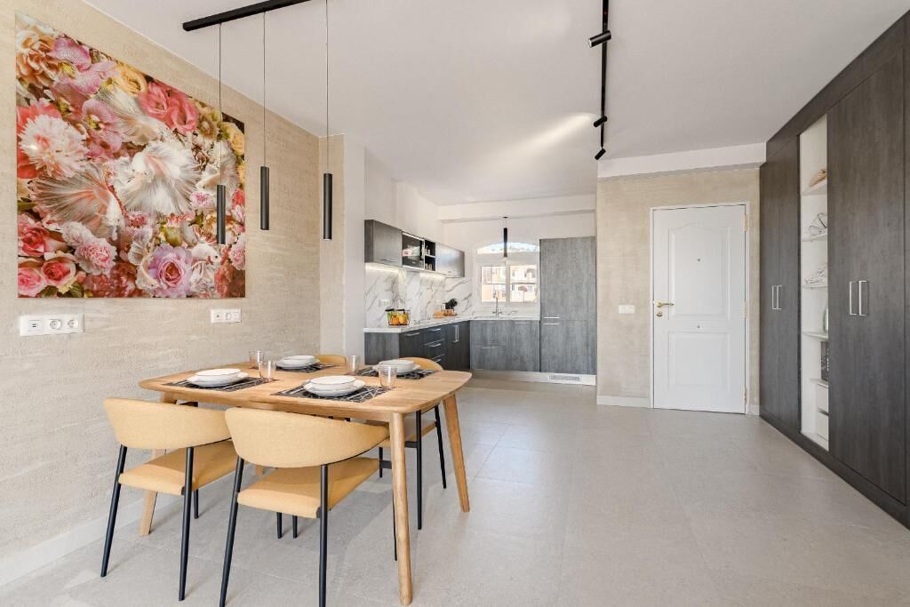 Eine moderne Küche mit Marmorarbeitsplatte, ein Essbereich mit Holztisch und -stühlen sowie ein großes Blumenbild an der Wand.