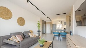 Un salon moderne avec un canapé gris, une table basse en bois et une cuisine en arrière-plan.