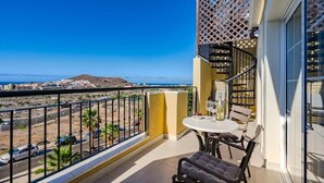 Un balcon avec une table et des chaises, une bouteille de vin et une vue sur la mer et les bâtiments éloignés.