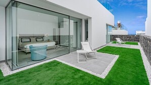 Una casa moderna con un dormitorio con paredes de vidrio, un patio con césped artificial y una pared de piedra.