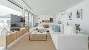 Una sala de estar moderna con un televisor grande, un sofá, una mesa de centro y una cocina al fondo.