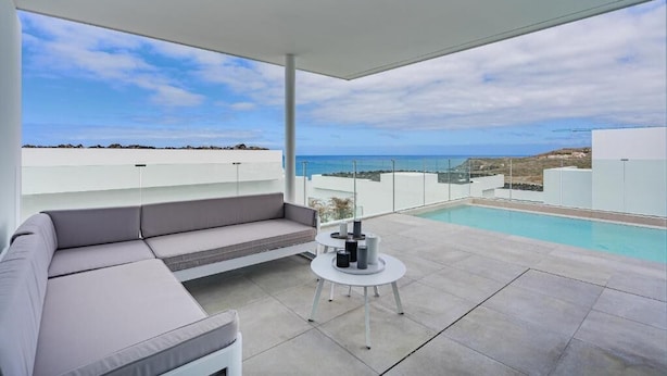 Un espacio exterior moderno con piscina, un sofá gris y una mesita con velas.