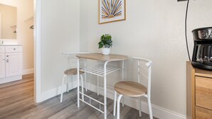 Pieni, käytännöllinen keittiönurkkaus, jossa on kahvinkeitin, pieni pöytä kahdella tuolilla ja ruukkukasvi.