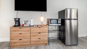 Pieni keittiönurkkaus, jossa on puinen kaappi, ruostumattomasta teräksestä valmistettu jääkaappi, mikroaaltouuni ja litteänäyttöinen televisio.
