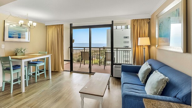 A room with a dining area, a sofa, a table, and a balcony with a view of the sea. - Caravelle Resort 606 (Myrtle Beach)