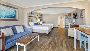 A compact hotel room with a sofa, two single beds, a wooden coffee table, a desk, and a bookshelf. - Caravelle Resort 606 (Myrtle Beach)