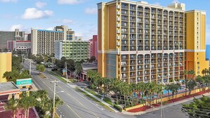 A multi-story hotel with a grid of balconies, a parking lot, and a swimming pool area. - Caravelle Resort 606 (Myrtle Beach)