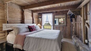 A rustic wooden room with a bed, a window with curtains, and a view of the outdoors. - Private and Historic Rocking Ox Ranchette & Estate (Fredericksburg)