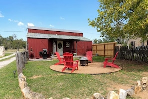 Une grange rouge dotée d’un espace de détente circulaire comprenant des fauteuils Adirondack rouges et un foyer.
