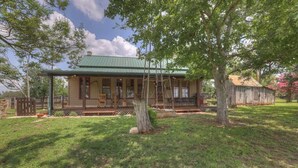 A rustic cabin with a green roof, surrounded by trees and a well-maintained lawn. - Private and Historic Rocking Ox Ranchette & Estate (Fredericksburg)