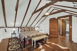 A bedroom with a sloped ceiling, a bed with a plaid bedspread, a wooden bench, and a cowhide rug.
