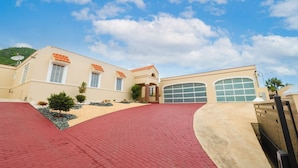 A two-story building with a red brick driveway, a garage, and a landscaped garden with small trees and shrubs.