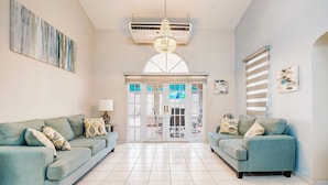 A spacious living room with two sofas, a chandelier, and a view through a glass door to an outdoor area.