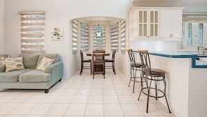 A dining area with a round table and chairs, a sofa, and a kitchen with white cabinets and a blue countertop.
