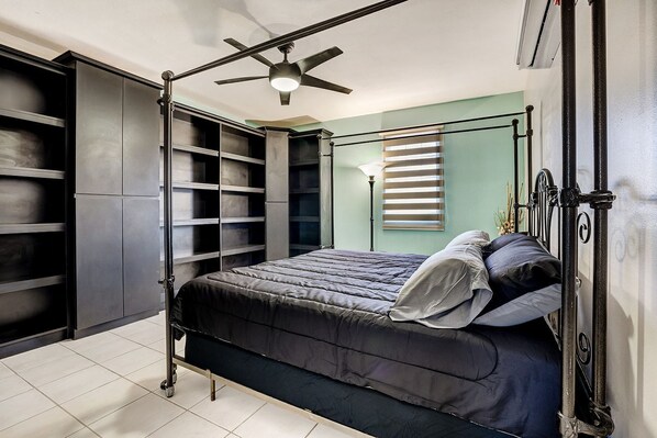 A bedroom with a bed, built-in shelving, a ceiling fan, and a window with blinds. - Dc Luxury House (Guayama)