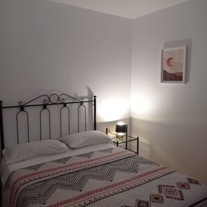 A single bed with a metal frame, a bedside table with a lamp, and a wall-mounted picture. - LA GAVIOTA (Tarajalejo)