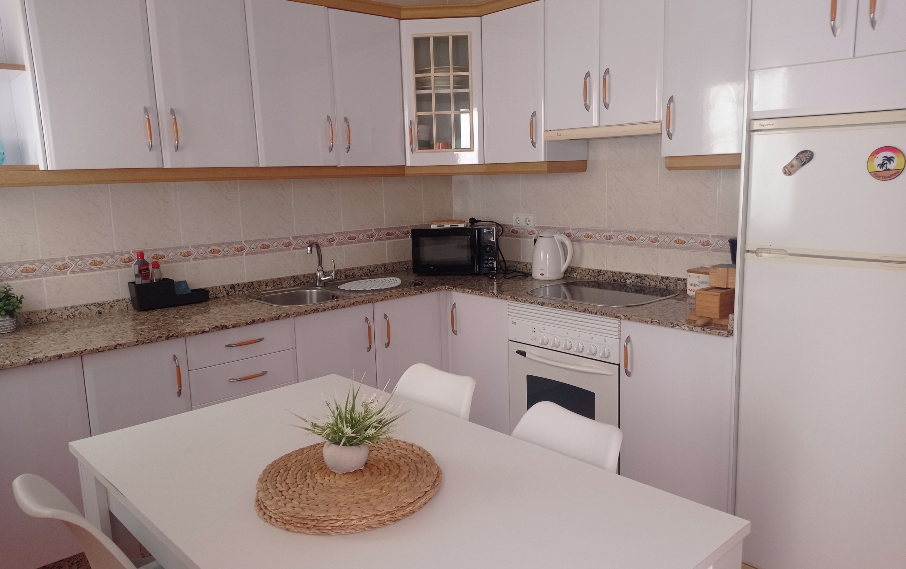 A kitchen with white cabinets, a microwave, a kettle, and a refrigerator.