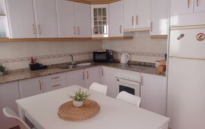 A kitchen with white cabinets, a microwave, a kettle, and a refrigerator. - LA GAVIOTA (Tarajalejo)