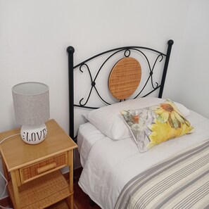 A bed with a wooden headboard, a white pillow, and a floral pillow. There is a bedside table with a lamp and a decorative item.