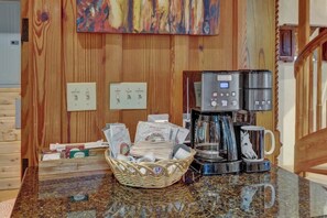 A coffee station with a basket of coffee packets, a coffee maker, and a mug on a granite countertop.