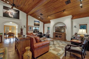 Amplia sala de estar con techos de madera, un televisor grande, sofás de cuero y piso a cuadros.