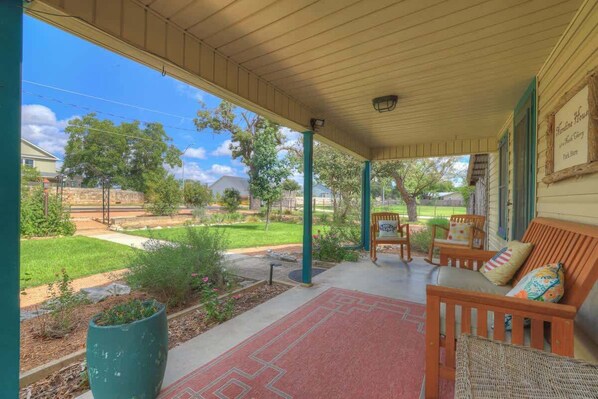 A covered porch with outdoor seating, a garden, and a view of a residential area.