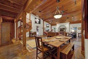 A spacious living area with a wooden dining table set for four, a staircase, and a fireplace. - Willows Retreat-Sleeps 17, Hot-Tubs,4 Mins to Main (Fredericksburg)