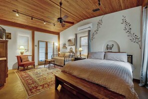 A bedroom with a wooden ceiling, a bed with a white bedspread, a bench, a chair, and a small table.