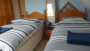 A bedroom with two beds, wooden headboards, a nightstand with a lamp, and a mirror. - Tower House
 (Helen's Bay)