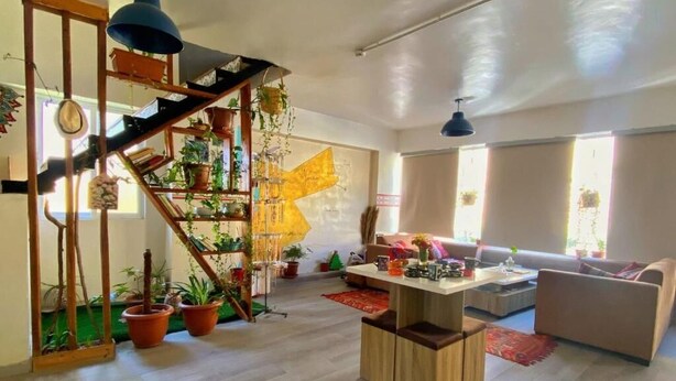 A spacious living room with a wooden staircase, a sofa, a coffee table, and a large window providing natural light. - The Castle Star (Amman)
