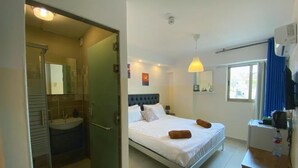 A bedroom with a bed, a bedside table, a mirror, a window with curtains, and a bathroom with a sink and mirror. - The Castle Star (Amman)