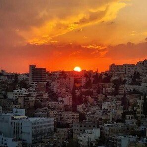 A cityscape at sunset with buildings silhouetted against a vibrant sky. - The Castle Star (Amman)