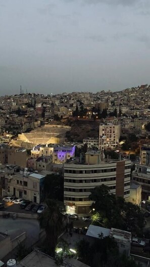 A cityscape at dusk with a prominent building featuring a large open area, possibly a public square or plaza, and several smaller buildings surrounding it. - The Castle Star (Amman)