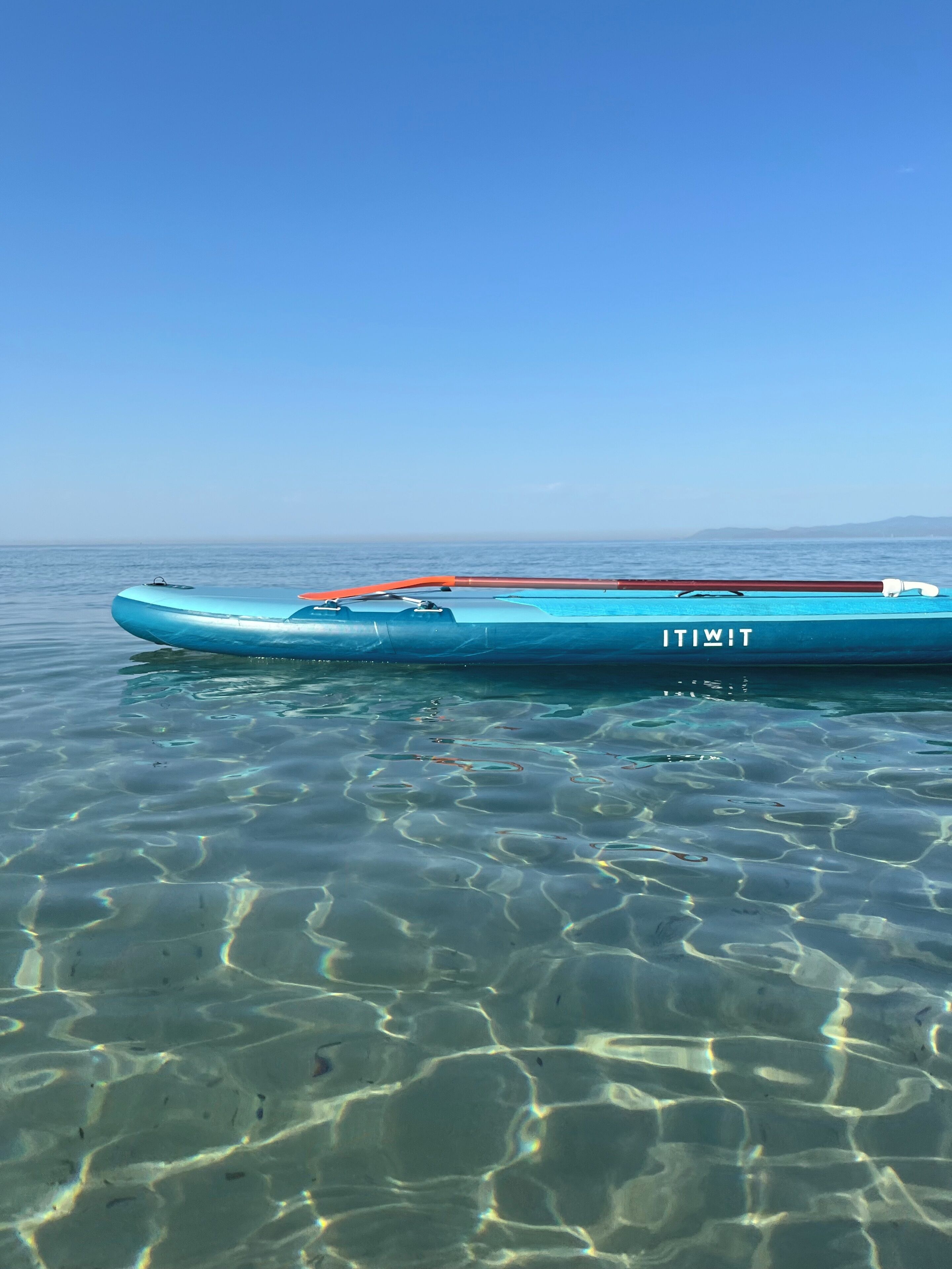 Ein klarer, blauer Himmel über ruhigem Wasser, mit einem Boot namens 'ITIWIT' auf der Oberfläche.