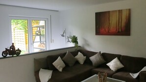 A living room with a brown sofa, a glass coffee table, and a window with a view of a building and greenery outside.