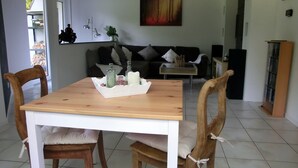 A dining area with a wooden table and chairs, a white cabinet, and a sofa in the background.