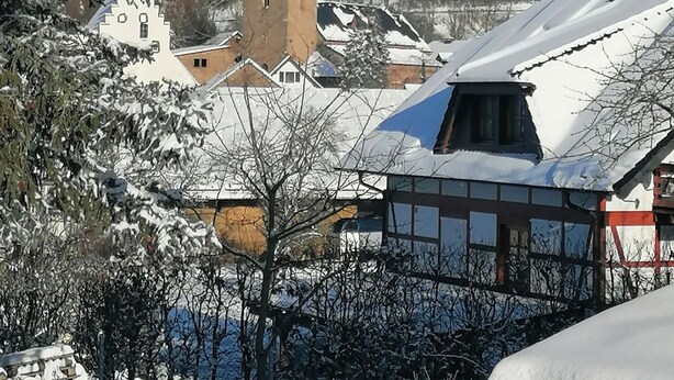 A snow-covered landscape with a church tower, buildings with traditional architecture, and a clear blue sky.