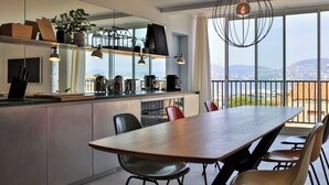 Eine moderne Küche mit einer großen Kochinsel, einem Essbereich mit Stühlen und Blick durch große Fenster.