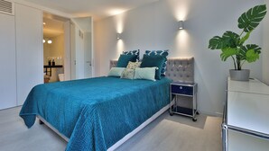 Ein modernes Schlafzimmer mit einem großen Bett, Nachttischen, einem Beistelltisch und einer Topfpflanze.