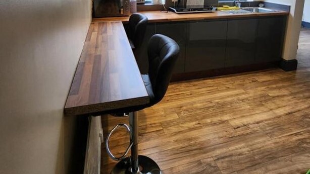 Una cocina moderna con una mesa de comedor de madera y un taburete negro, horno empotrado y un ventanal grande.