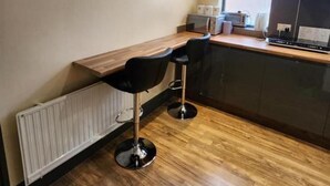 Una cocina compacta con encimera de madera, dos taburetes negros tipo bar, un microondas integrado y una ventana que proporciona luz natural.