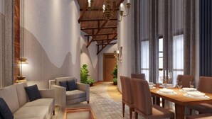 Une salle à manger spacieuse avec un plafond haut et des poutres apparentes, un coin salon confortable avec des canapés et une table dressée pour un repas, ainsi que de grandes fenêtres avec des rideaux.