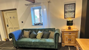 Um sofá verde com várias almofadas, um armário de madeira, um tapete estampado, uma janela com cortinas e uma parede com um letreiro em nuvem de palavras.
