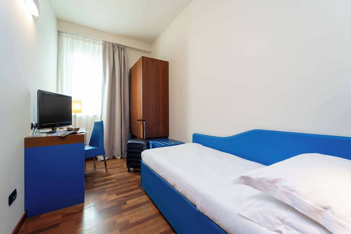 A hotel room with a bed, a desk with a computer, a chair, and a wardrobe.