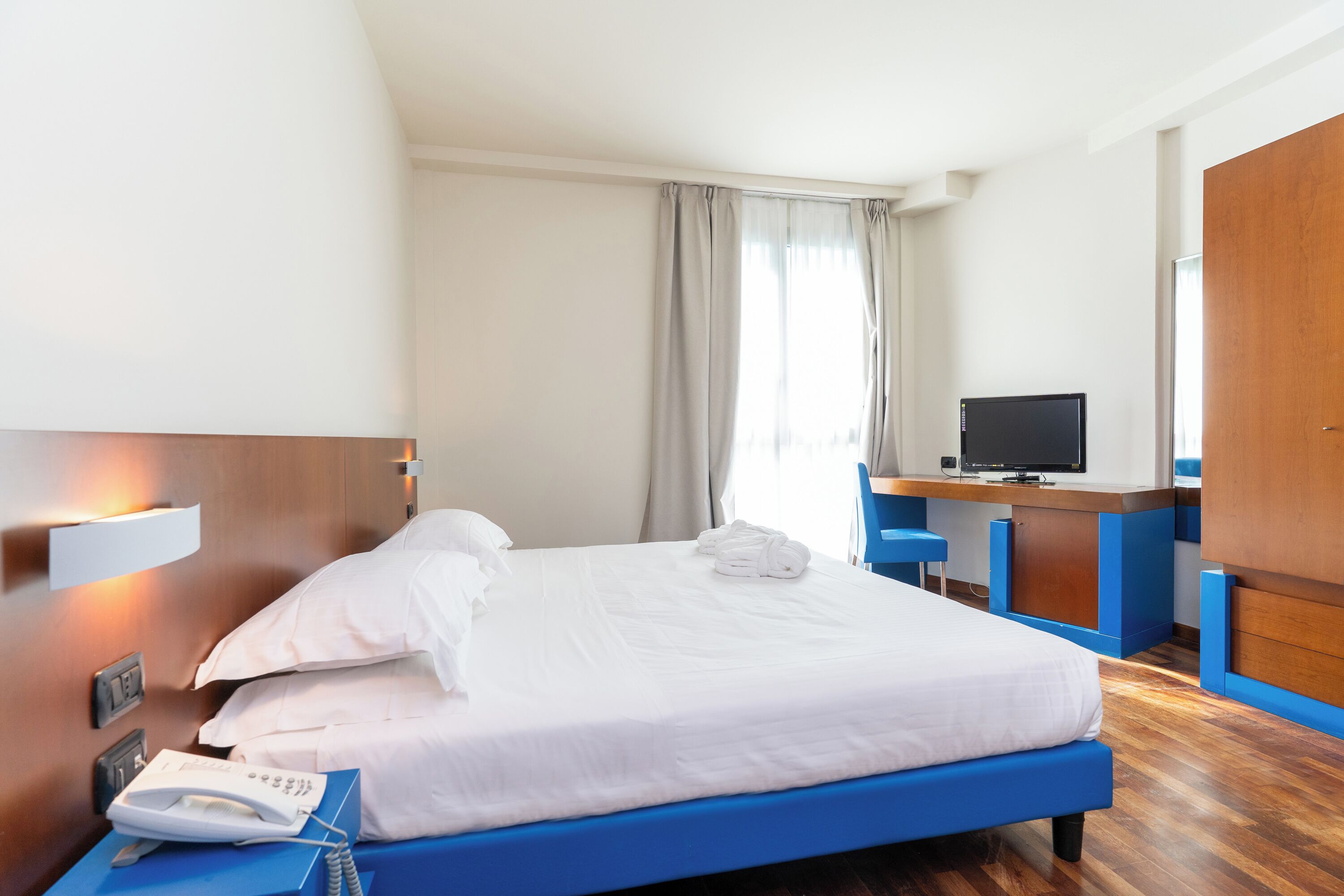 Une chambre d’hôtel équipée d’un lit, d’un bureau, d’une télévision et d’un téléphone.
