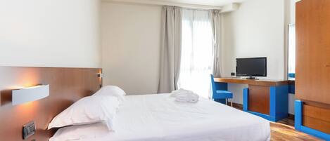Une chambre d’hôtel équipée d’un lit, d’un bureau, d’une télévision et d’un téléphone.