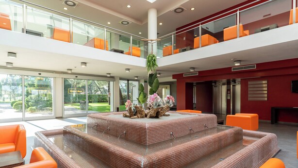Un vestíbulo moderno con una zona de estar central, barandillas de vidrio y una escalera.