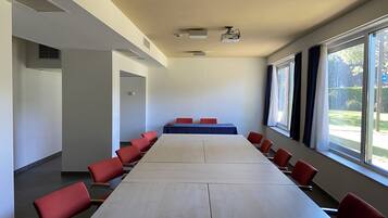 Een vergaderzaal met een lange tafel en rode stoelen, grote ramen en een projecteerder aan het plafond.
